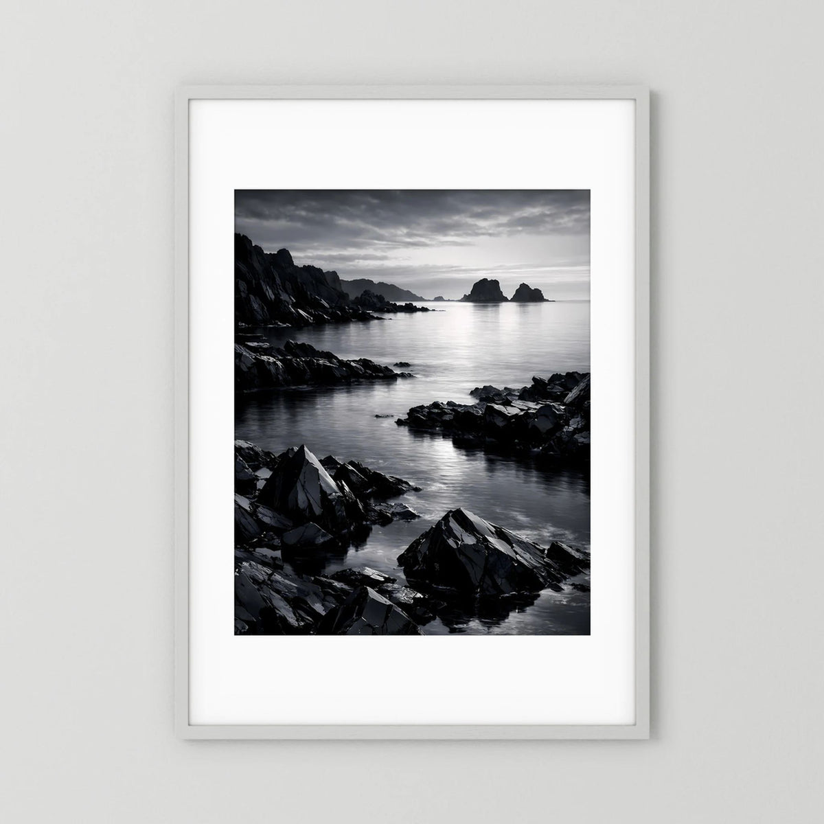 Wandbild in Schwarzweiß mit felsiger Küste und ruhigem Meer, weißer Rahmen