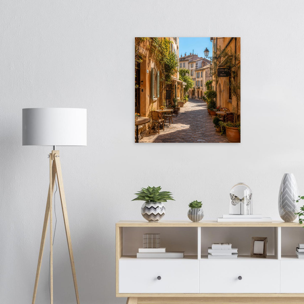 Poster: Blick in eine schmale Gasse mit Tischen, Kübeln und üppigem Grün an den Häusern