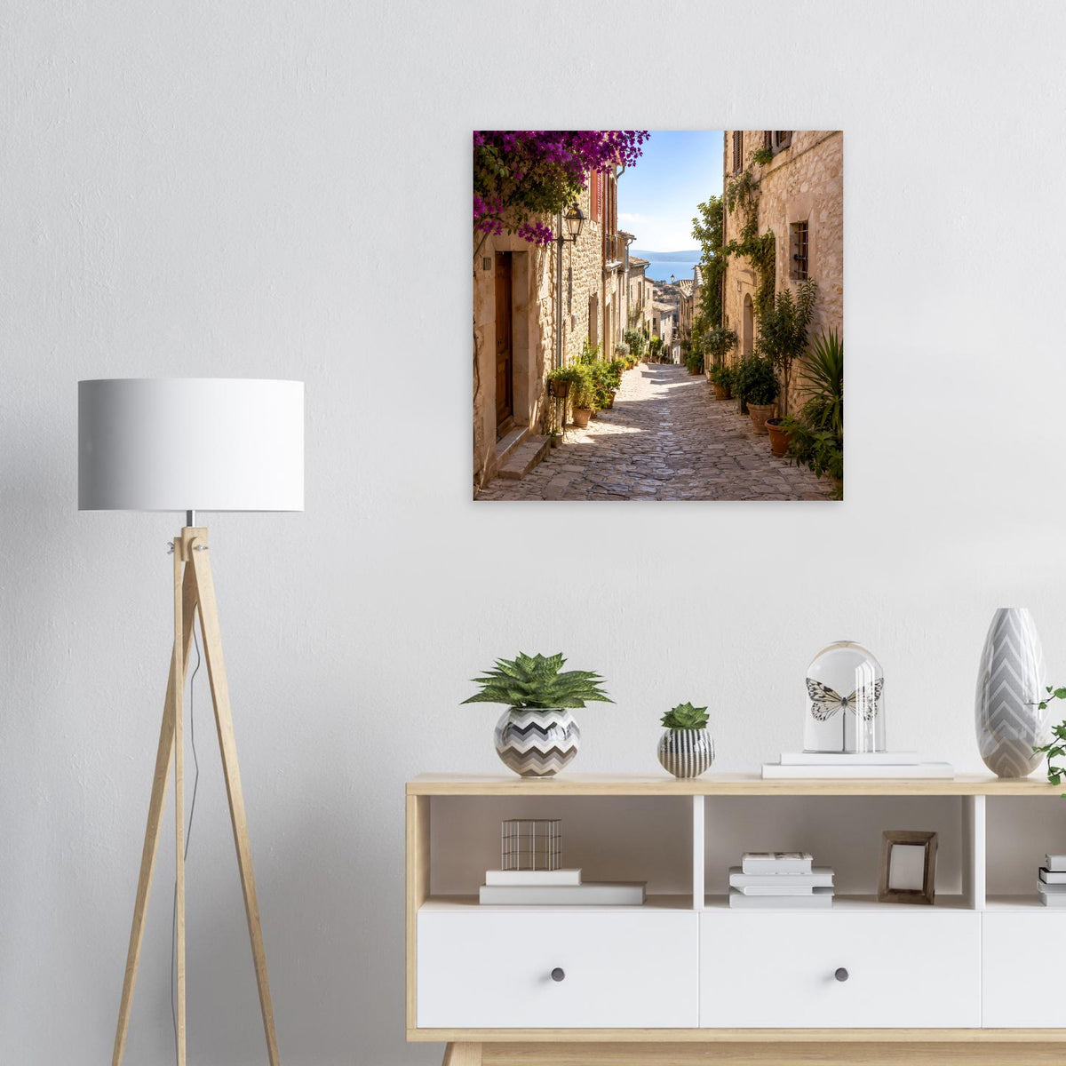 Quadratisches Poster mit Gassenblick zwischen Steinhäusern, Pflanzen und lila Blüten