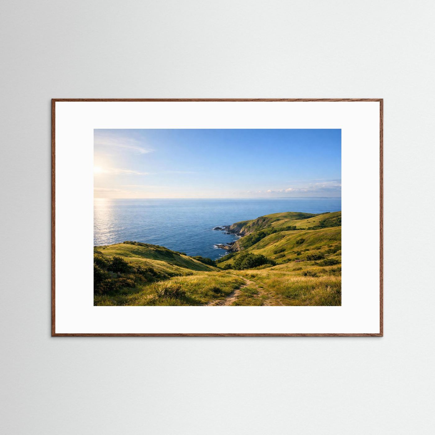 Poster mit Küstenlandschaft im Sonnenlicht, dunkler Holzrahmen und weißer Rand