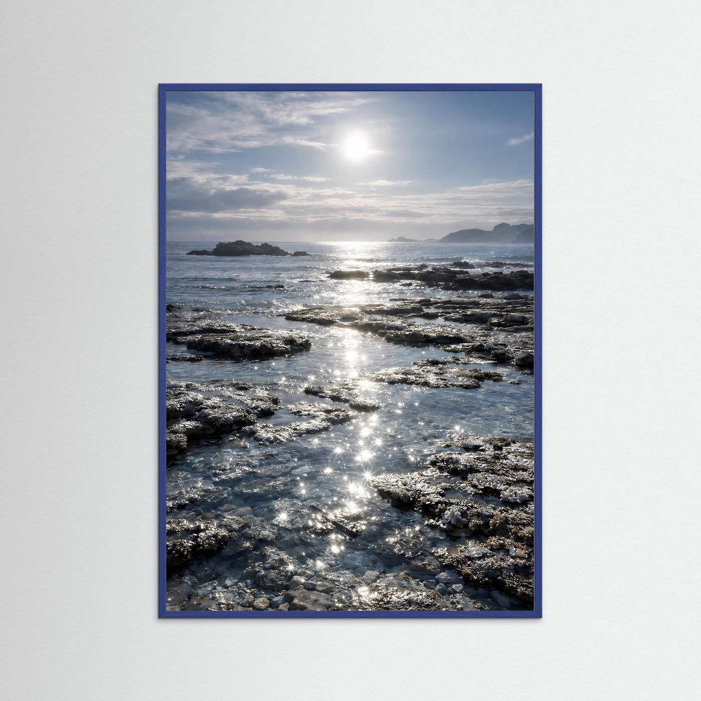 Küstenposter im Hochformat mit blauem Rahmen, Felsen und Sonnenreflexen im Meer