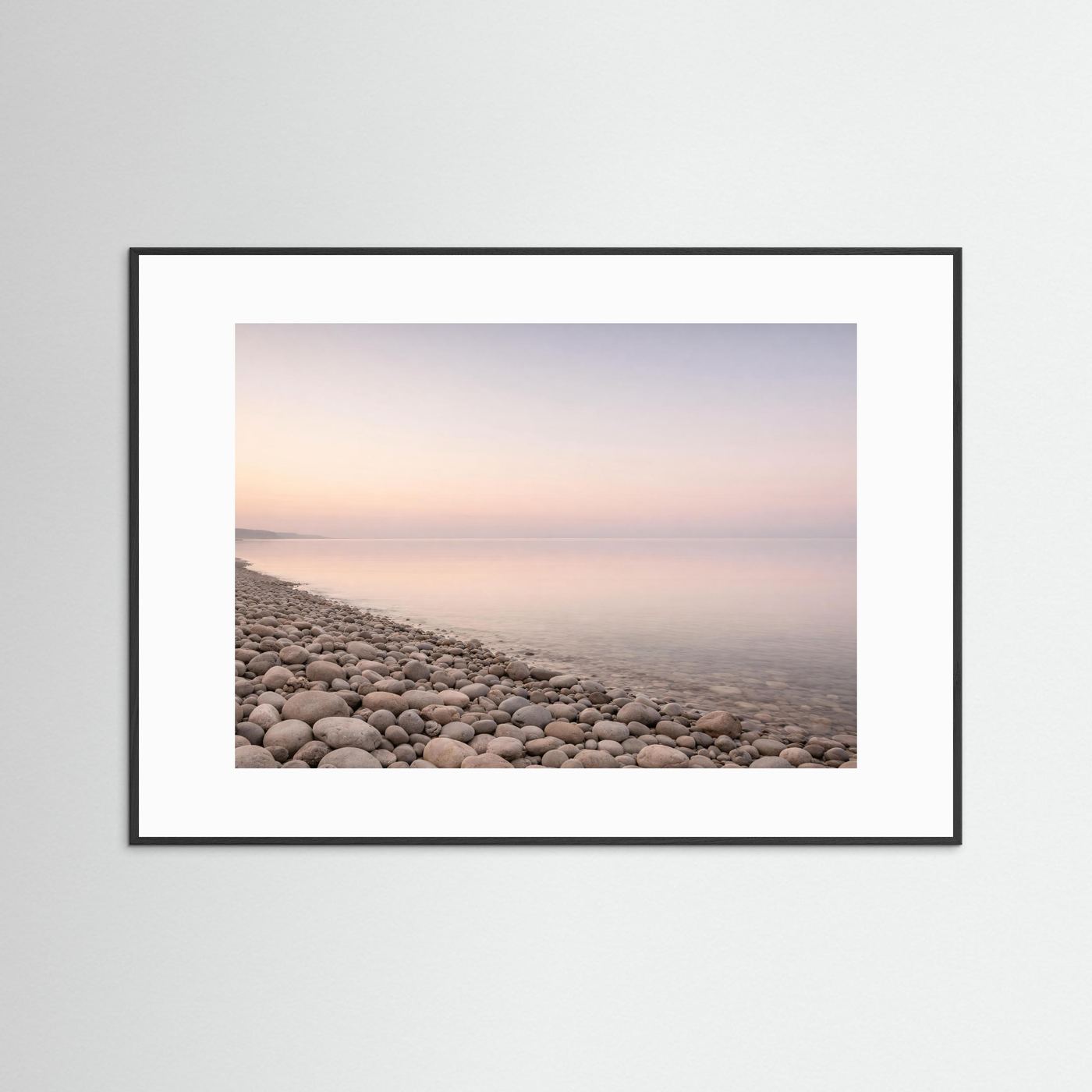 Panorama-Poster Kiesstrand und Meer im Pastelllicht, schwarzer Rahmen mit weißem Passepartout