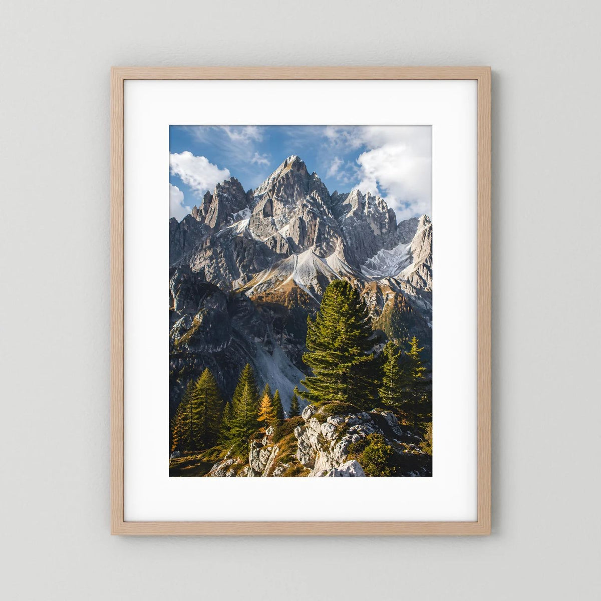 Poster mit hellem Holzrahmen und weißem Passepartout: Alpen-Gipfel und Tannen im Hochformat.