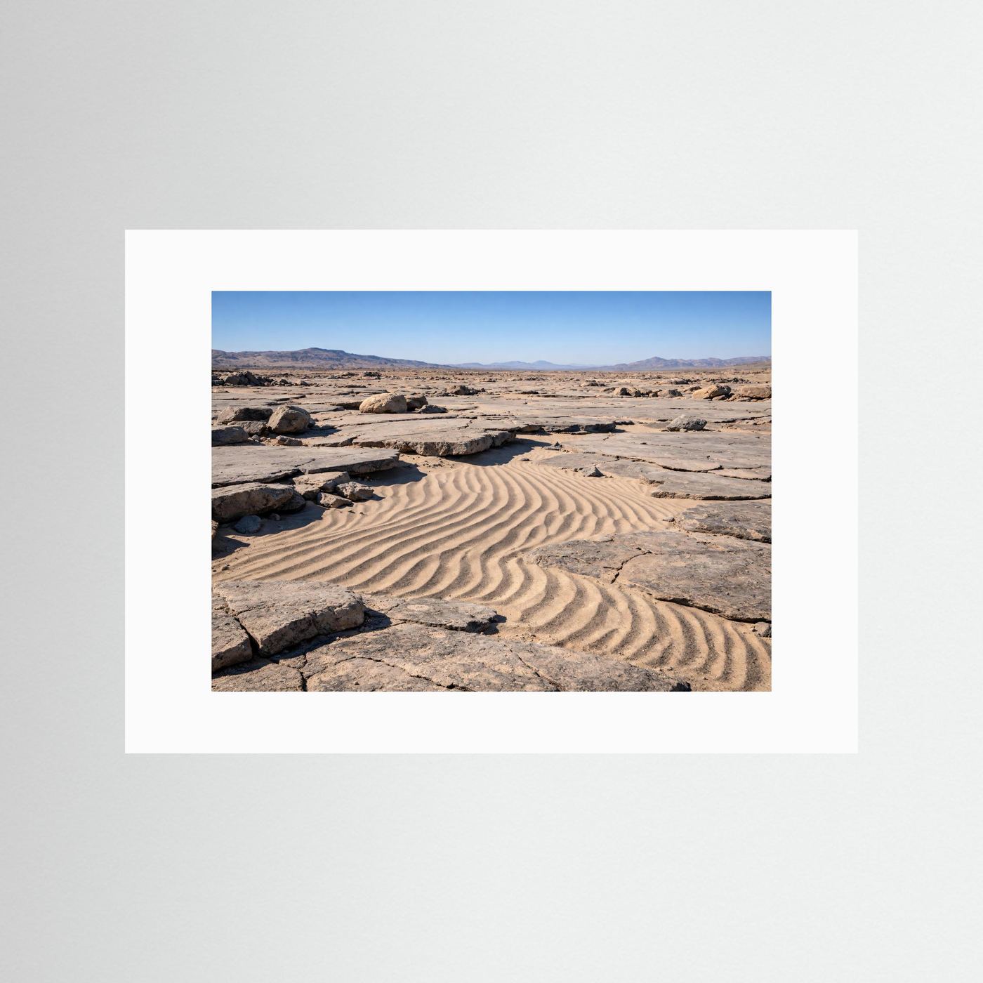 Naturposter im Querformat mit weißem Rand: Sanddünen und Felsbrocken in der Wüste