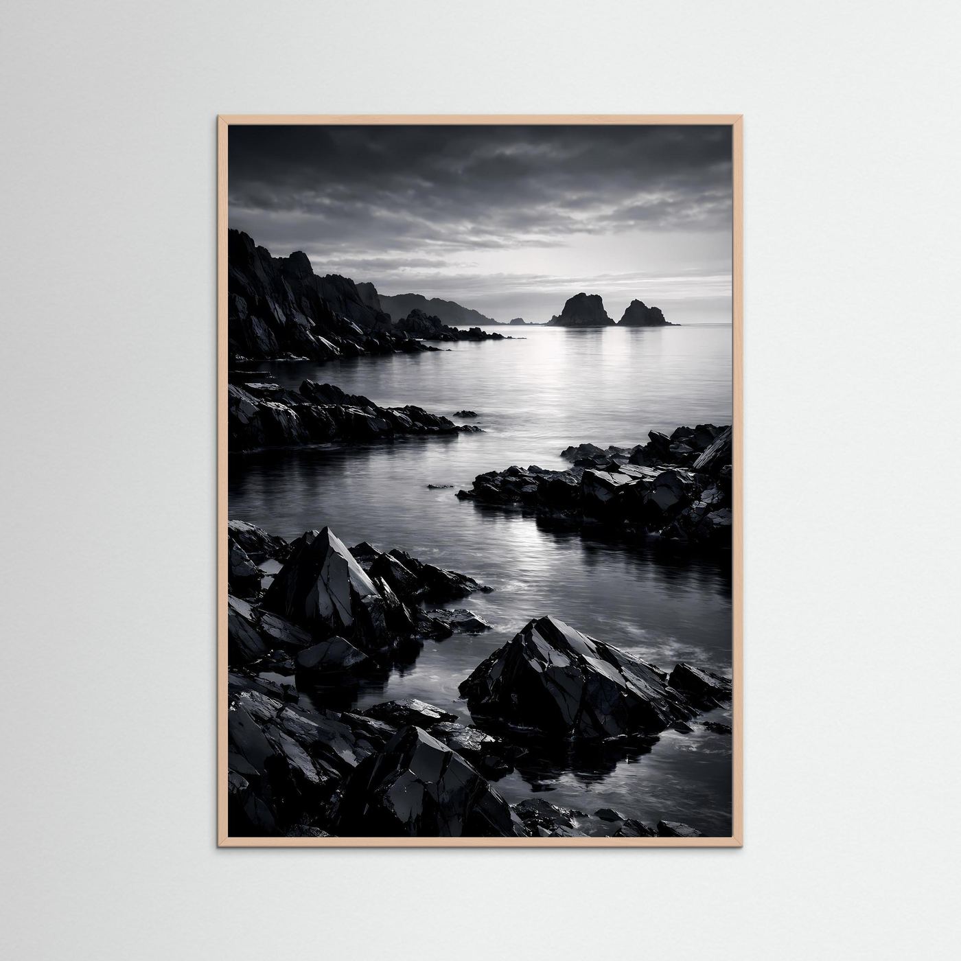 Wandbild Schwarz-Weiß-Küste mit Felsen am Wasser, Himmel mit Wolken; heller Holzrahmen