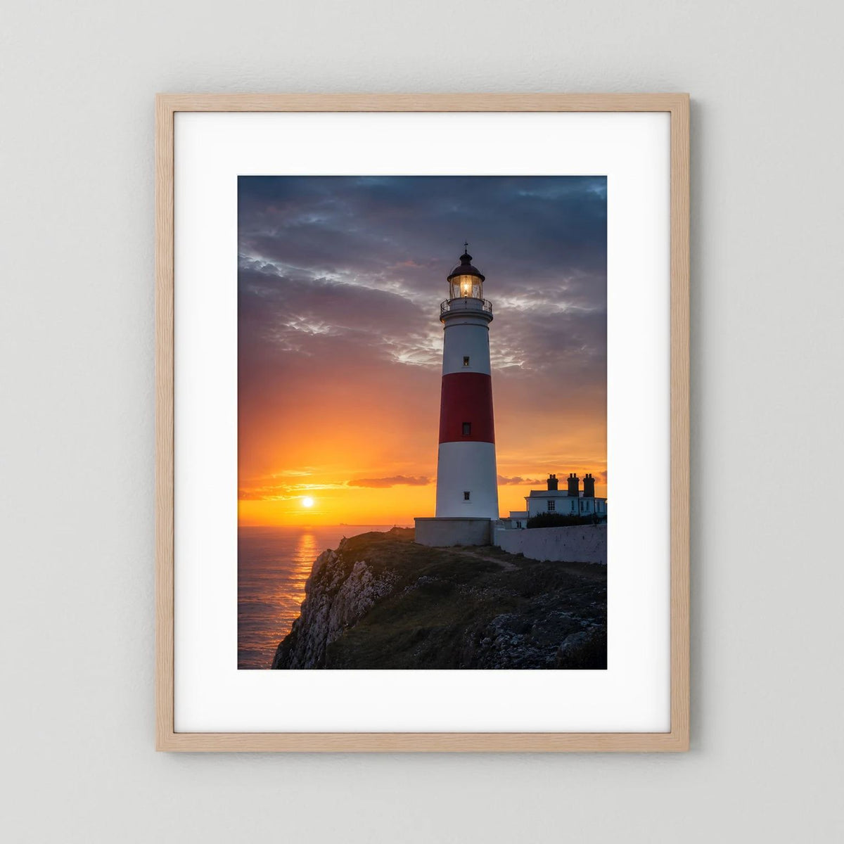 Wandposter mit Leuchtturm am Meer bei Sonnenuntergang, heller Holzrahmen mit weißer Einfassung
