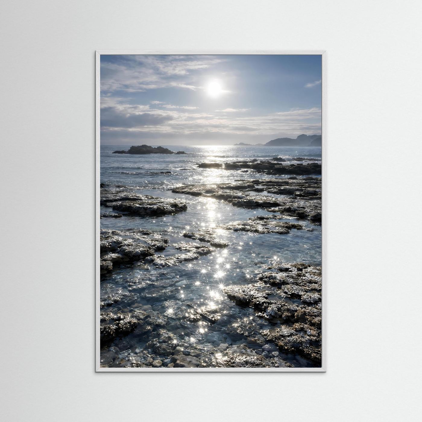 Küstenposter im Hochformat mit silberfarbenem Rahmen und Sonnenreflexen auf Felsenriffen