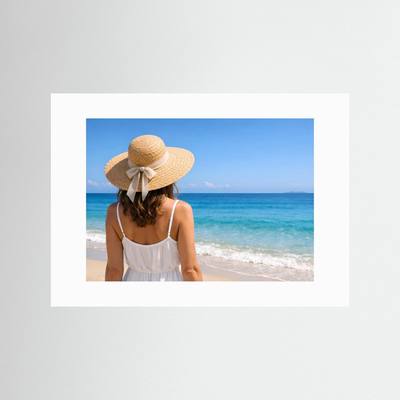 Strandposter im weißen Passepartout: Frau mit Strohhut im weißen Kleid, Blick auf das Meer