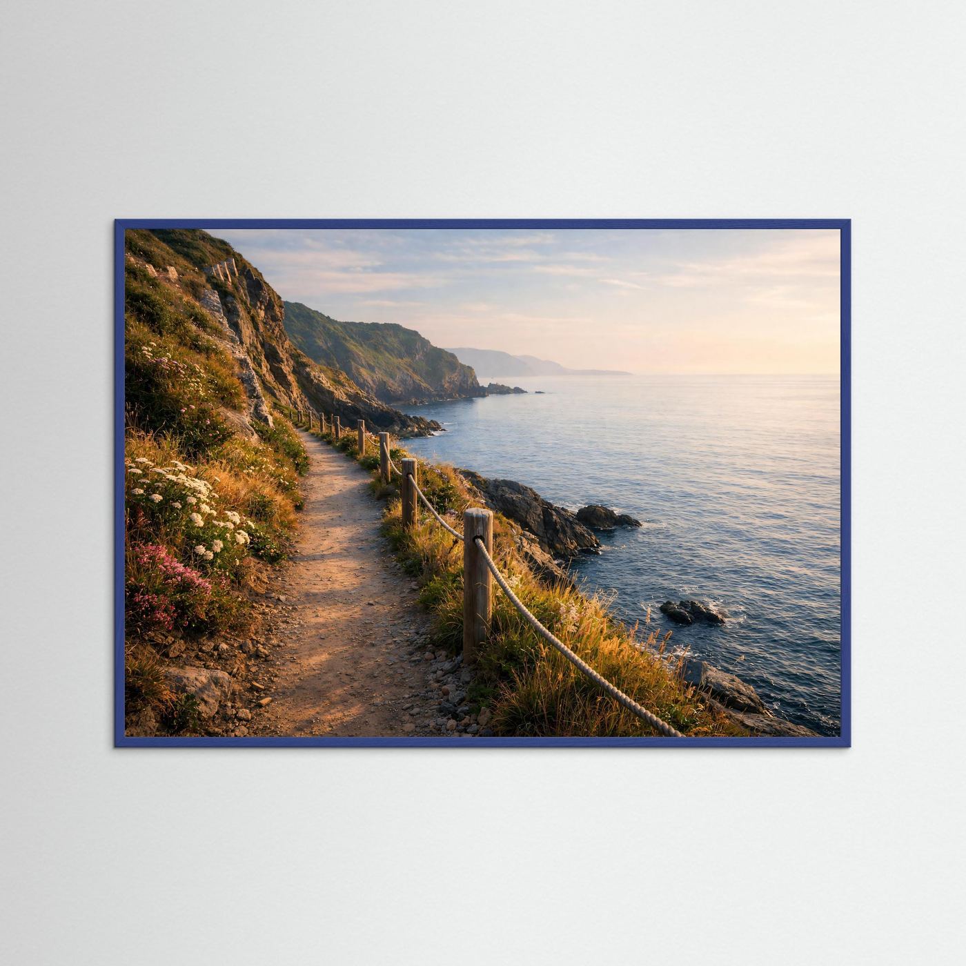 Wandposter mit Küstenpfad am Meer entlang, Felsen und Ufergeländer; blauer Rahmen.
