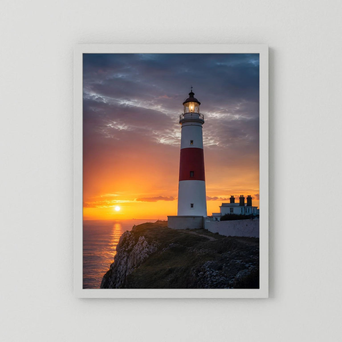 Wandposter mit Leuchtturm am Meer bei Sonnenuntergang, weißer Rahmen
