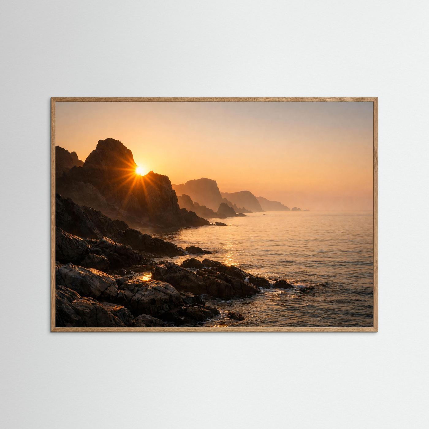 Poster im Querformat mit Sonnenaufgang an der felsigen Küste und Meer, heller Holzrahmen