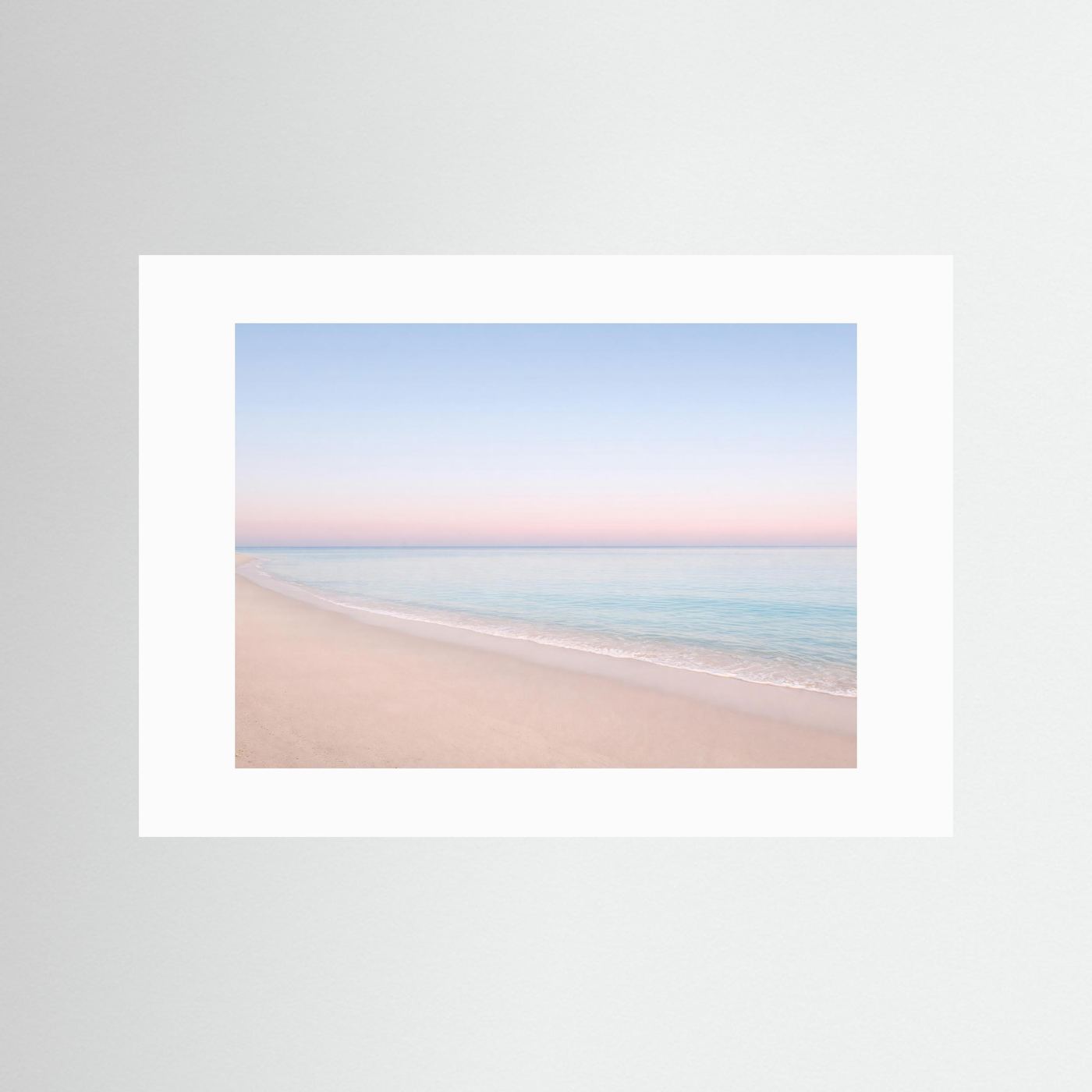 Strandposter im Querformat mit weißem Passepartout, Sandstrand und rosa-blauem Himmel