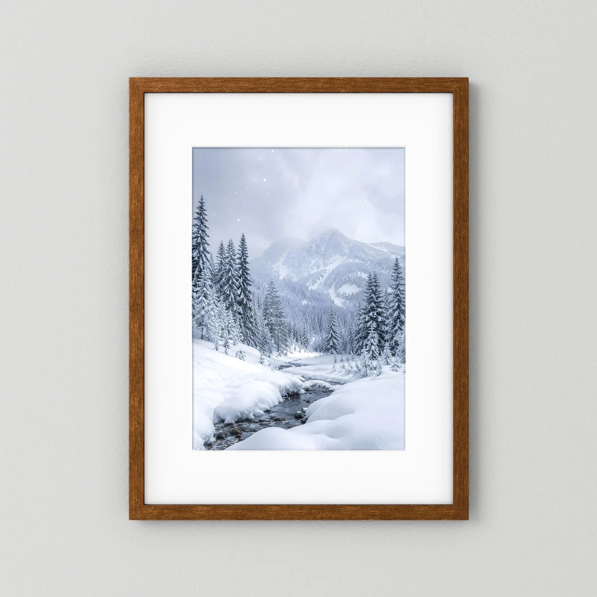 Winterlandschaft-Wandbild mit braunem Holzrahmen und weißem Passepartout: verschneite Berge und Tannen.
