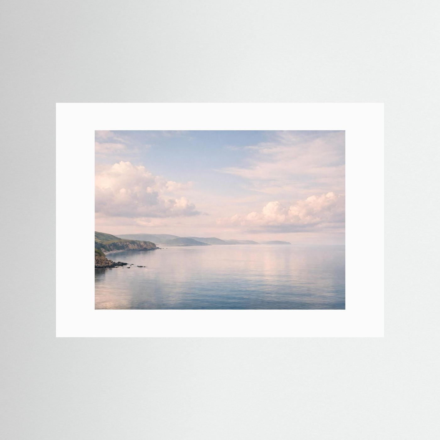 Querformatiges Panorama-Meerposter mit weißem Rand: ruhige Bucht, Küste und Wolken