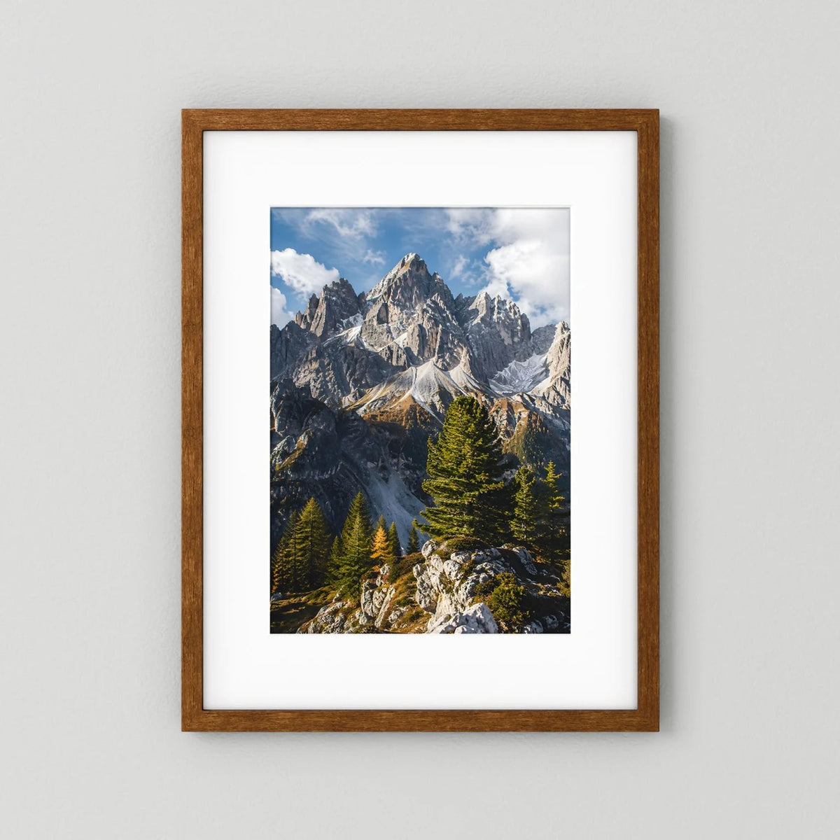 Poster mit braunem Holzrahmen und weißem Passepartout: Alpenberge und Tannen im Hochformat.