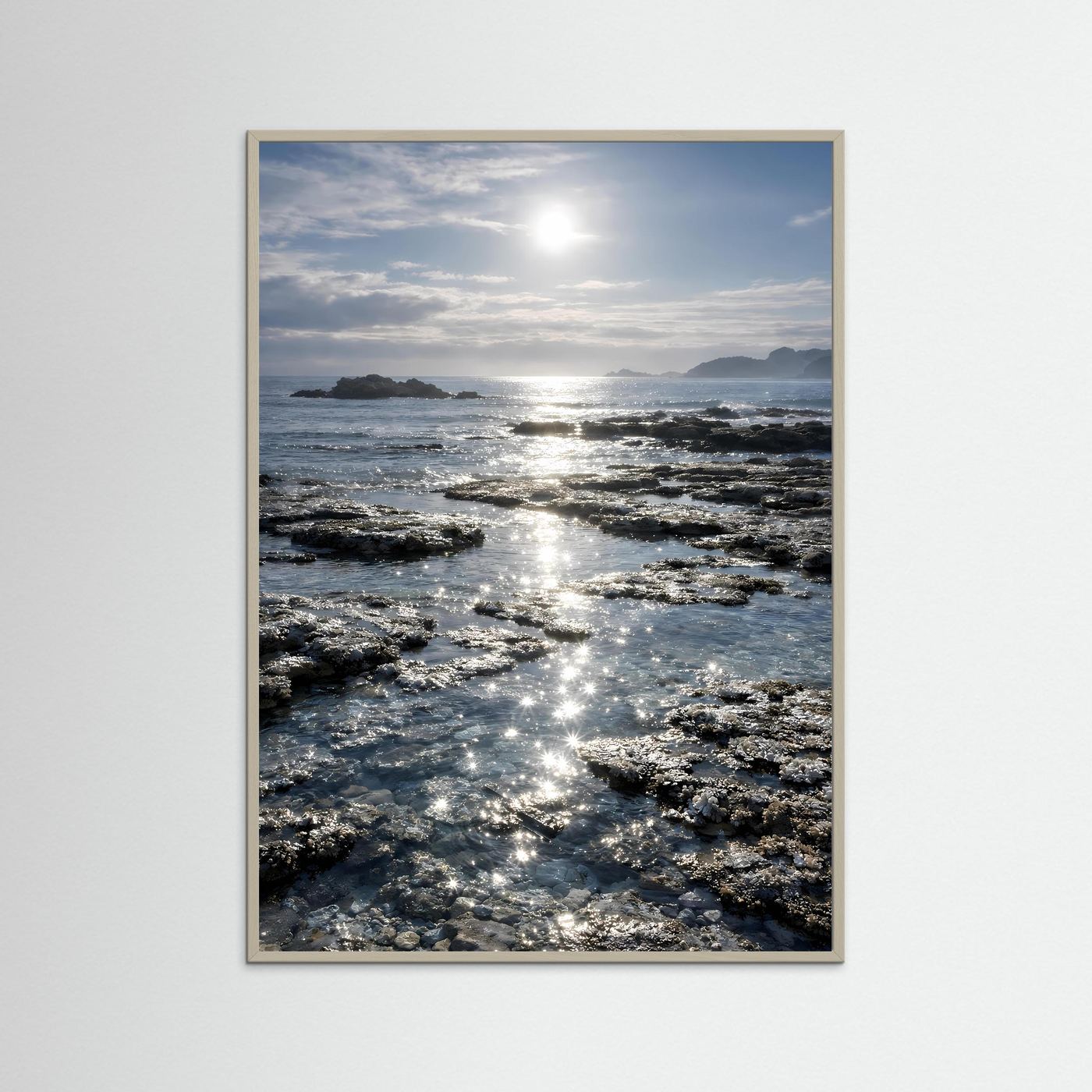 Küstenposter im Hochformat mit beigem Holzrahmen, Felsen und Sonnenreflexe auf Wellen