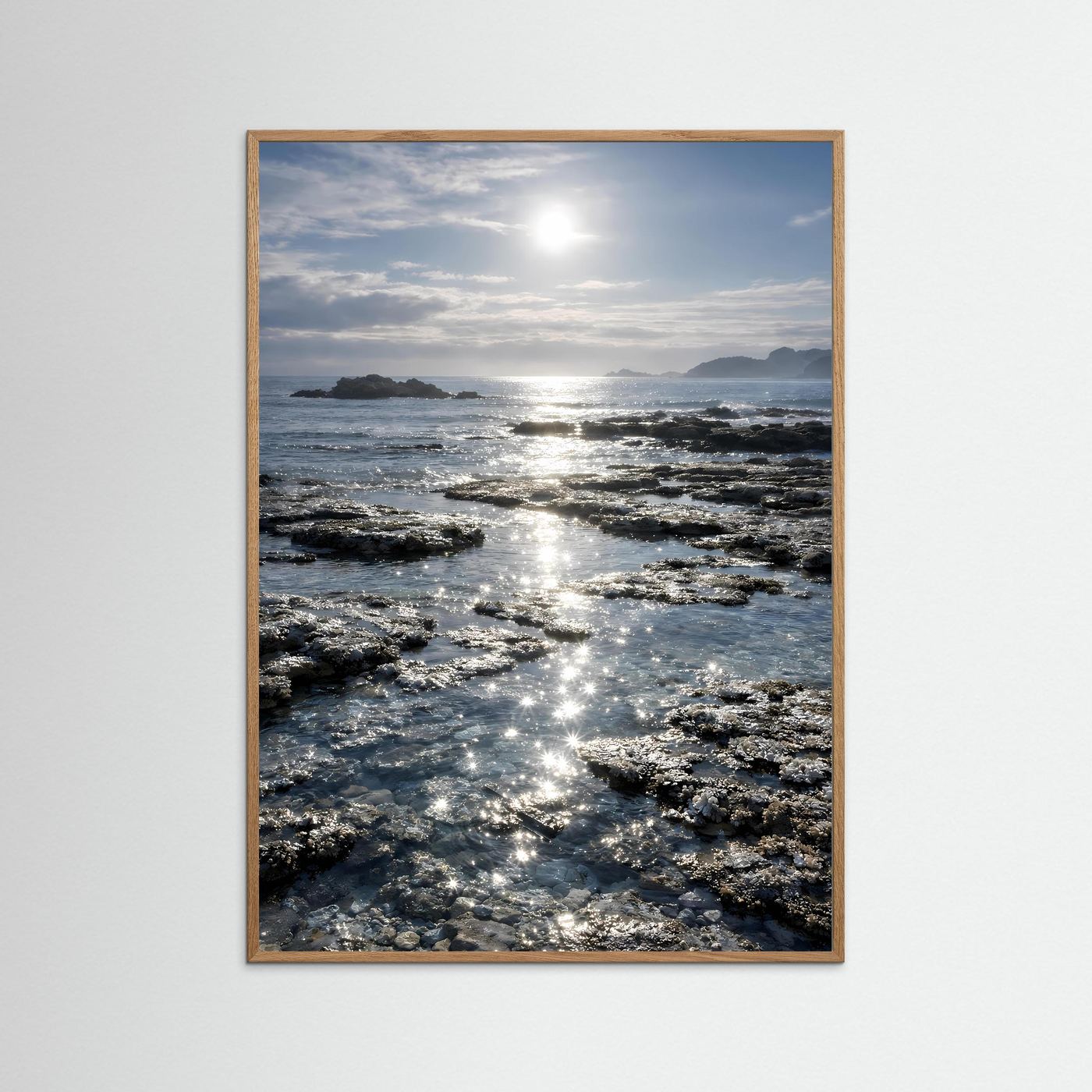 Küstenposter im Hochformat mit hellbraunem Holzrahmen, Felsen und Sonnenreflexen
