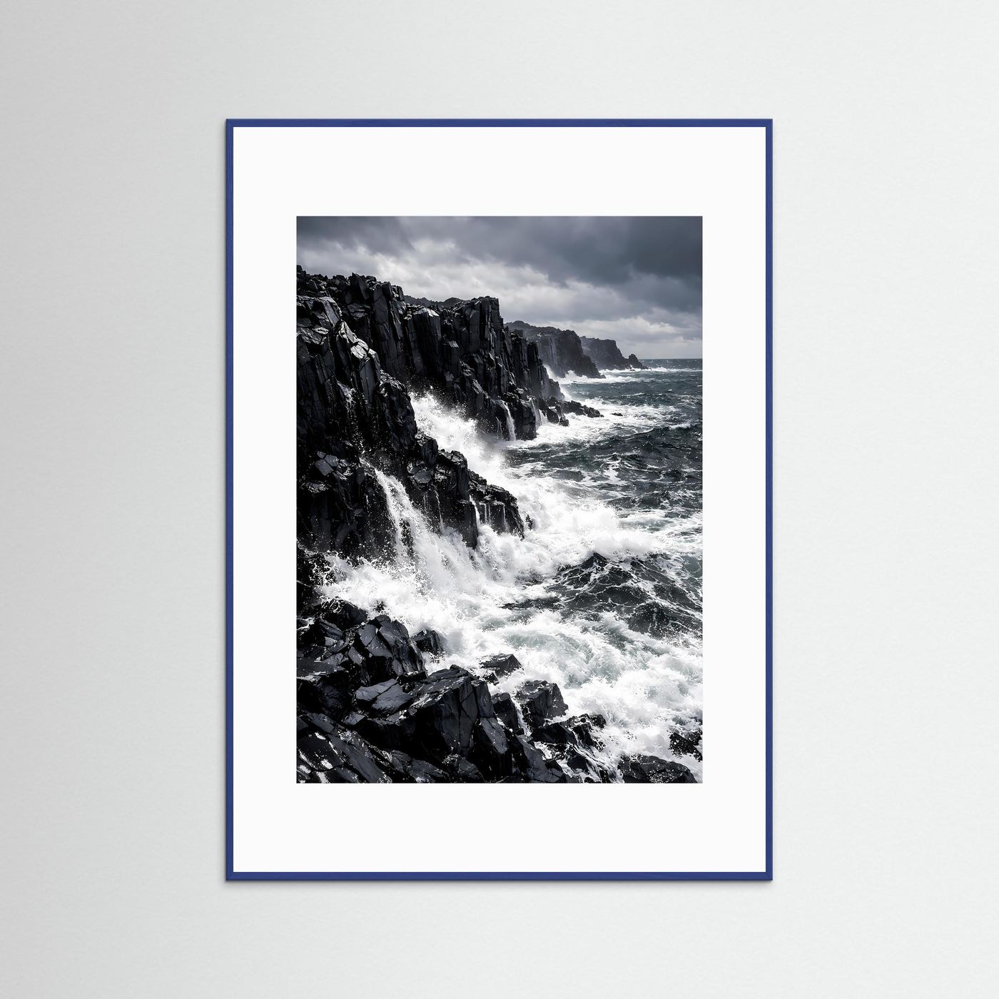 Wandbild im Hochformat mit Meerblick, schwarzen Klippen und weißen Gischtwellen im blauen Rahmen