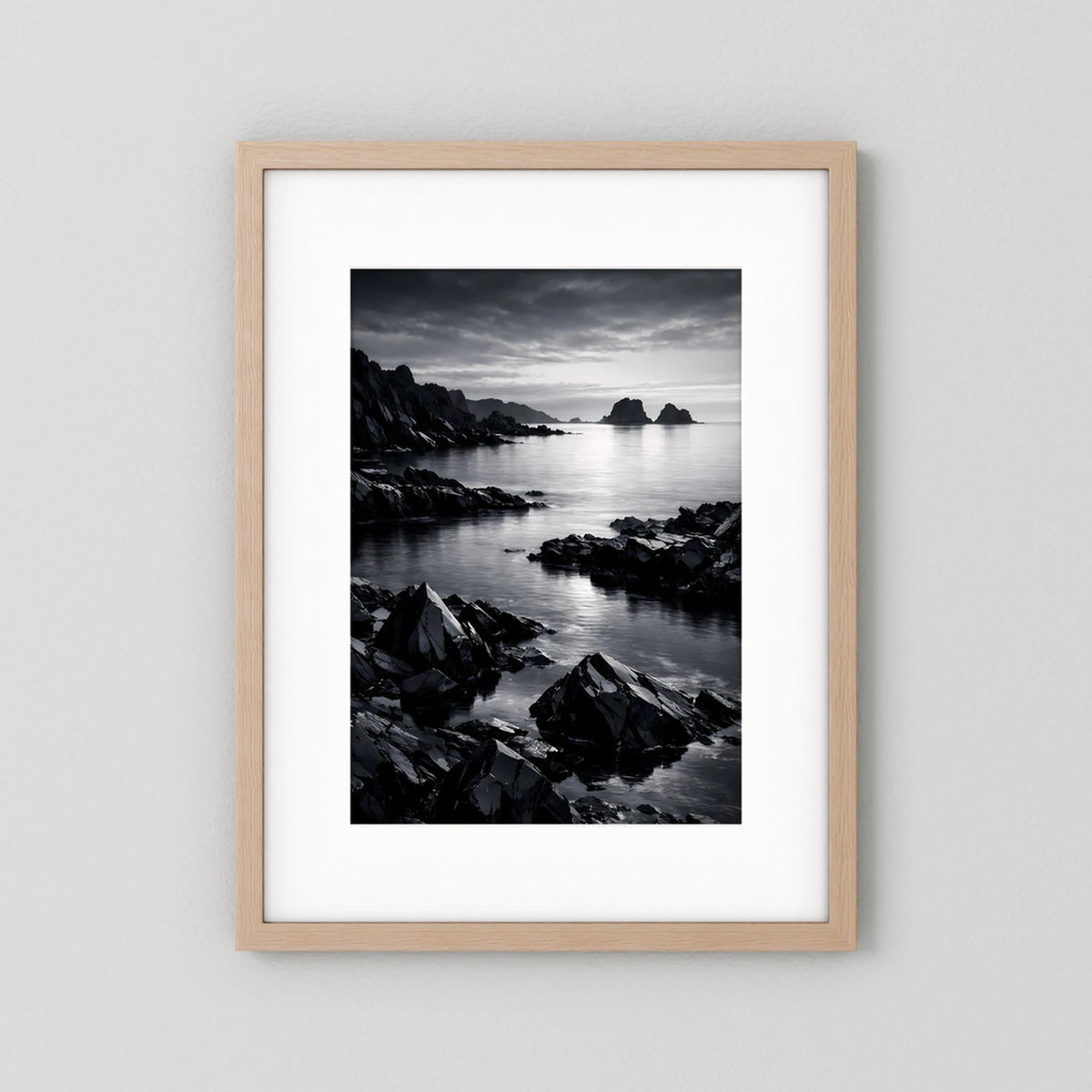 Wandbild in Schwarzweiß mit felsiger Küste und ruhigem Meer, Holzrahmen hell